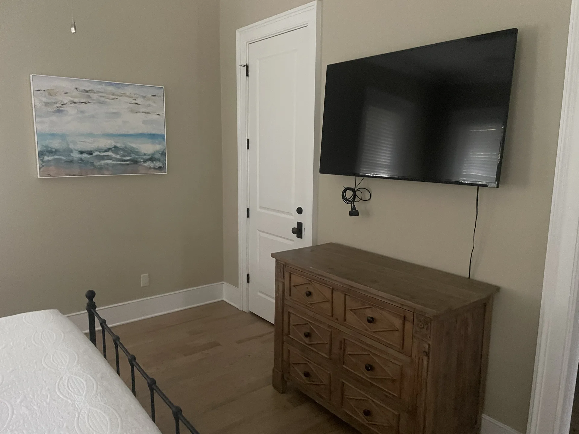 Bedroom with iron frame bed, ocean wave artwork, wall-mounted TV, and rustic dresser