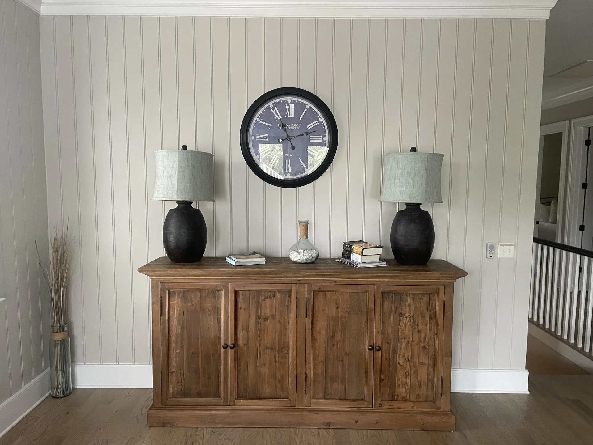 Entry console with rustic wood sideboard, twin lamps, and vintage wall clock against beadboard