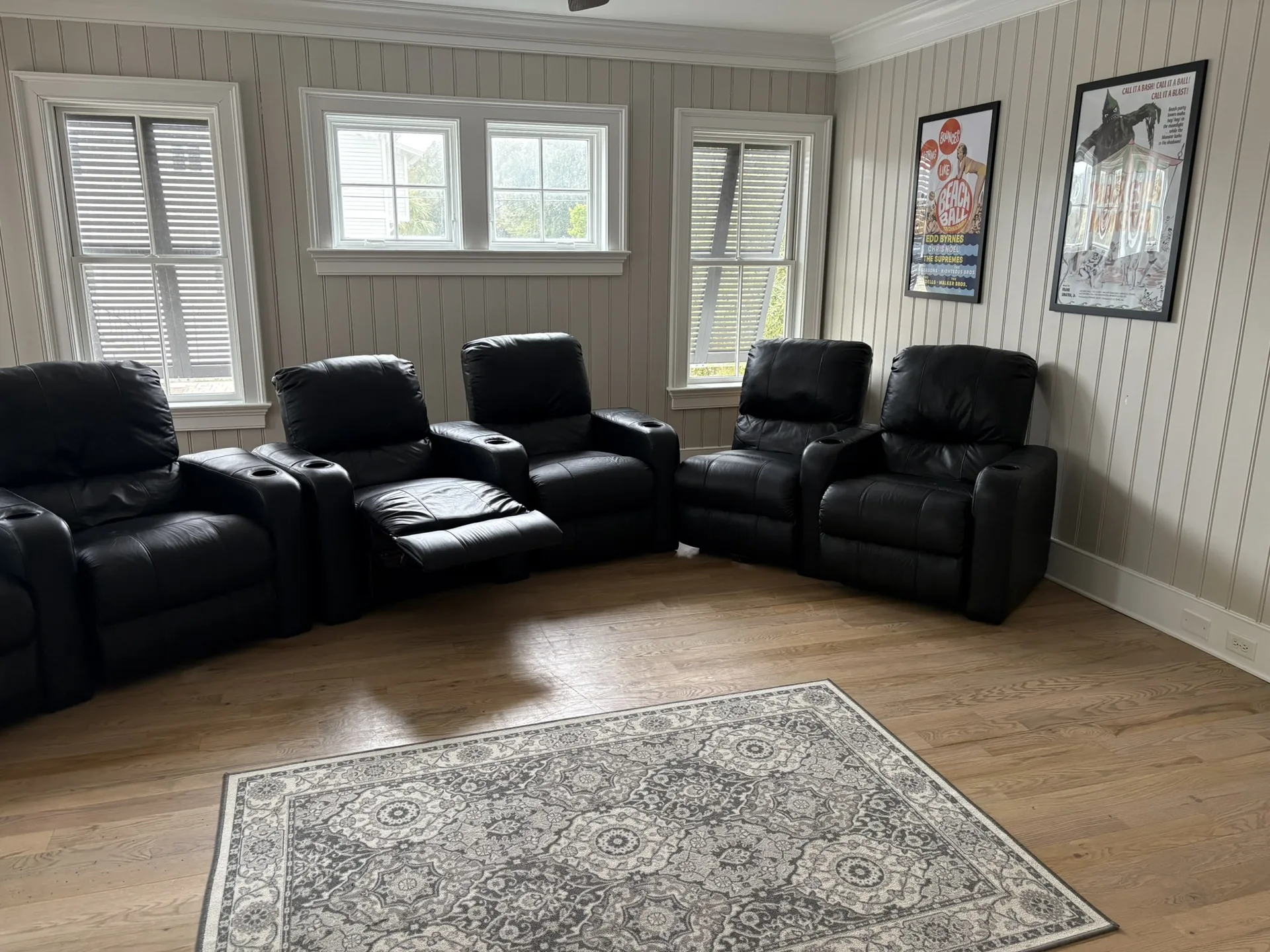Home theater room with four black leather recliners and movie posters on beadboard walls