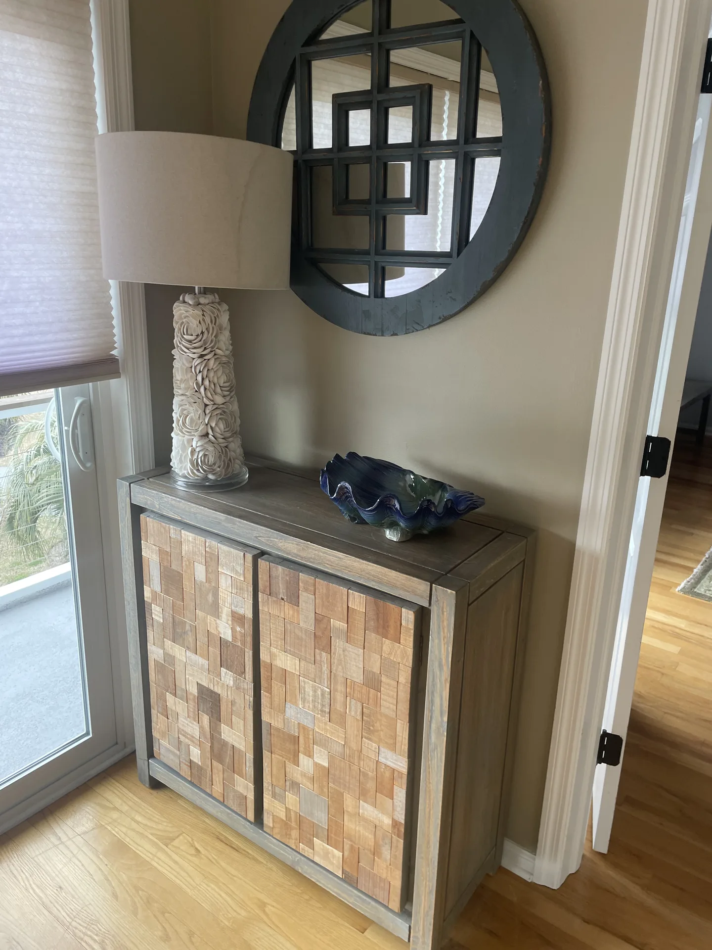 Entryway accent cabinet with mosaic doors, coastal lamp, and round mirror